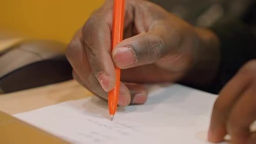 Closeup Hands Signing Document with Orange Pen Laptop and Mouse Nearby Seal Impression Subtle Formal