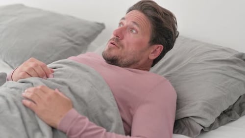 Homme d'âge moyen mal à l'aise faisant des cauchemars en dormant dans son lit