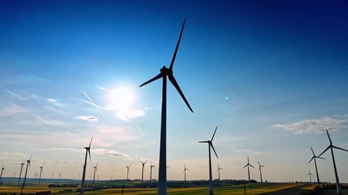 Turbines create green energy rural. Rows of wind turbines stand tall against a bright blue sky