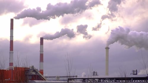 Factory with smoking chimneys against background of clouds and sunset sky.