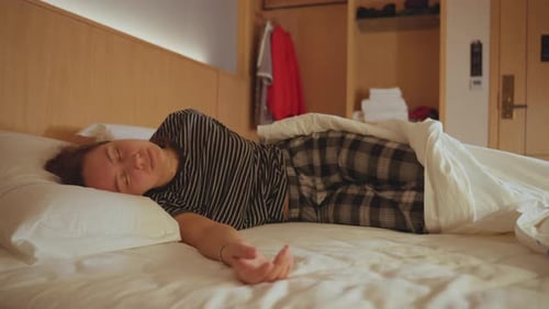 Woman in Pajamas Stretches in Hotel Bed