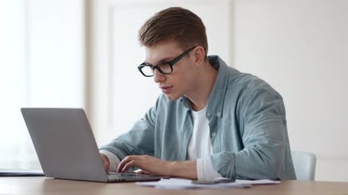 Young Guy Watching Tutorials Online on Laptop at Home Office