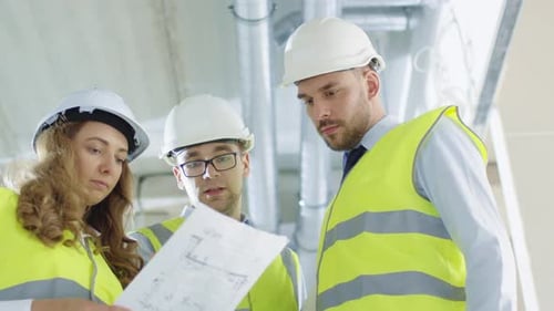 Team of Engineers in Hard Hats Having Conversation, Looking at Blueprint, inside Building Under Con