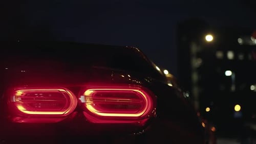 Black Sports Car Tail Light Glowing in the Dark of a Night City