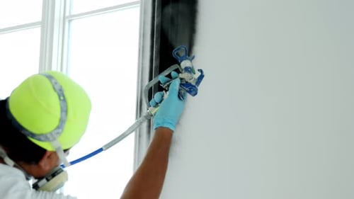 Painter Spraying Wall Black in Brightly Lit Room