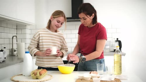 Teen girl and woman baking in bright kitchen