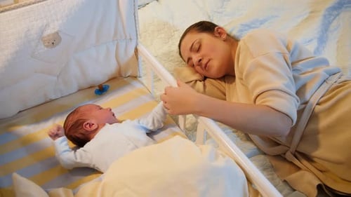 Mother Sleeping Near Newborn Infant in Crib