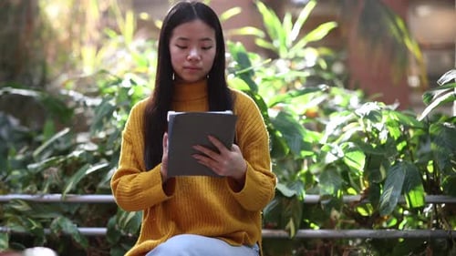 pretty asian woman in the park sitting using digital tablet