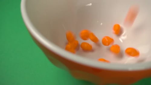 Lateral view of orange skulls shaped candy falling on a plate.