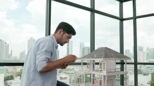 Man Reviews Blueprints Beside House Model in Office