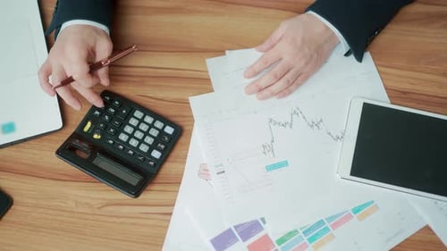 hands close up of financial analyst accountant at desk counting report on calculator with documents