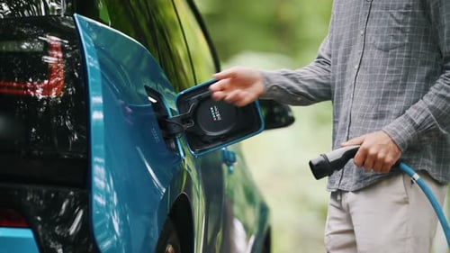 Young man charging electric car outdoor at green forest. Save ecology alternative energy sustainable