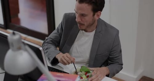 Adult male having lunch whilst working at desk in office