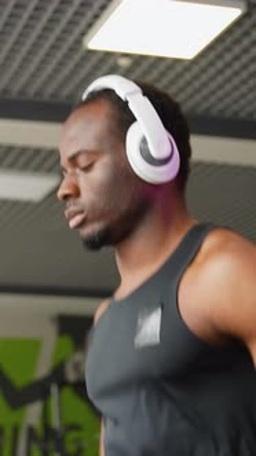 A Man with Headphones Running in a Modern Gym on a Treadmill Vertical Video
