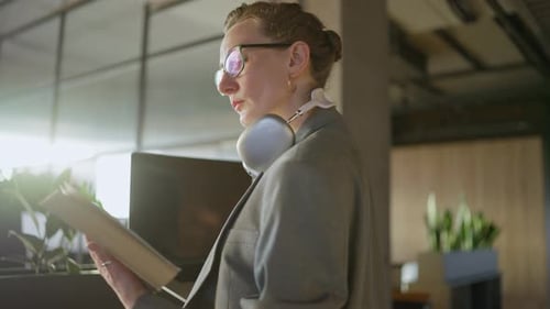 Middleaged Blonde Businesswoman with Glasses in a Gray Business Uniform Stands in the Office and