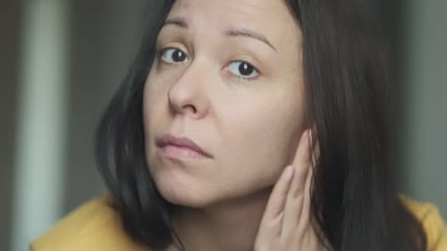 Frustrierte Frau untersucht ihr Gesicht im Spiegel und betrachtet vergrößerte Poren, Pigmentierung und Falten