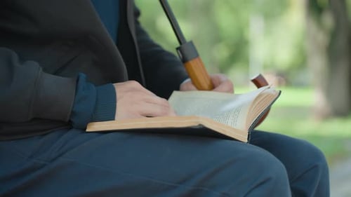Man reading book, sitting with umbrella in park
