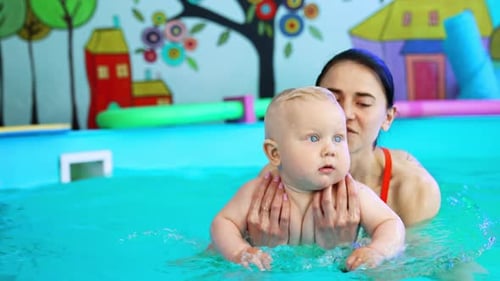 Brunette woman dipping a little kid in the water of swimming pool and lifting up.