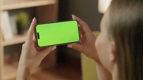 Woman Holding a Modern Smartphone with a Bright Green Screen Horizontally Using Both Hands While