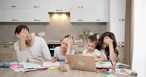Tired Parents Help Children Do Homework at Table in Kitchen