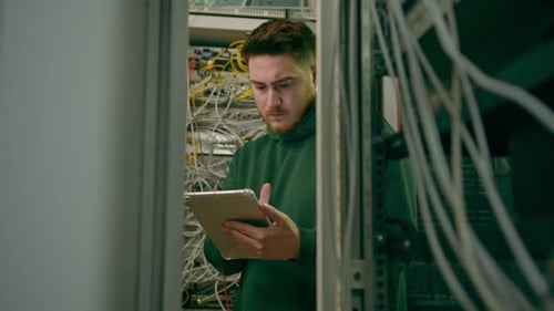 Hacker or engineer in data center holding tablet steals software or checks information from server