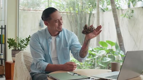 Homme tatoué tenant un serpent dans les mains tout en travaillant à la maison