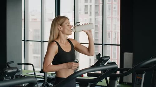 Woman Drinking Water on Treadmill at the Gym