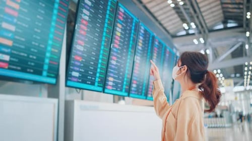 Asian woman traveler checking flight schedule board in airport terminal