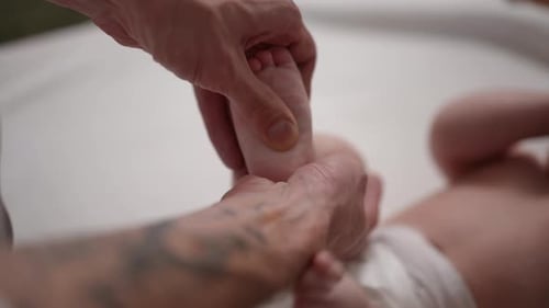 Gentle Hands Massage Tiny Infant Foot on White Sheet