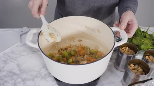 Person Stirring Vegetables in a White Pot