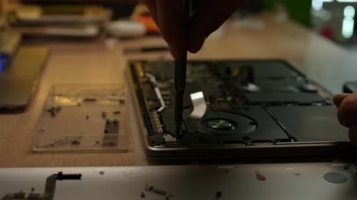 Nahaufnahme eines Technikers, der das Laptop-Motherboard mit einem Schraubenzieher repariert, der von verschiedenen Komponenten umgeben ist