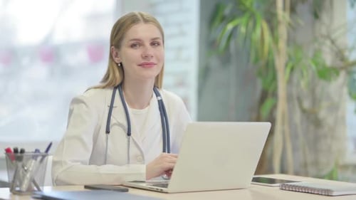 Friendly Young Woman Doctor Works on Laptop