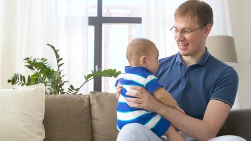 Father Holding Infant on Couch in Bright Home