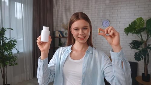 Woman Displays Vitamin Capsule and Bottle Indoors