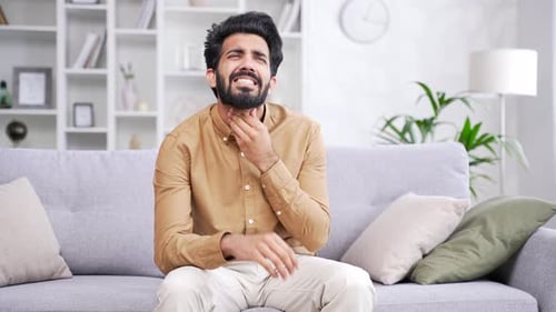 Young Man Massaging Sore Throat in Living Room