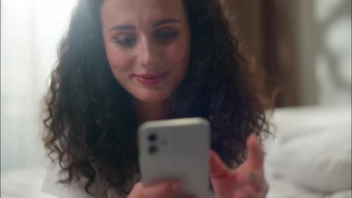 Smiling Woman Using Smartphone in Bedroom