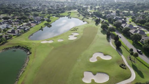 Slow rising drone shot of lush green golf course in Florida senior living community during sunrise.