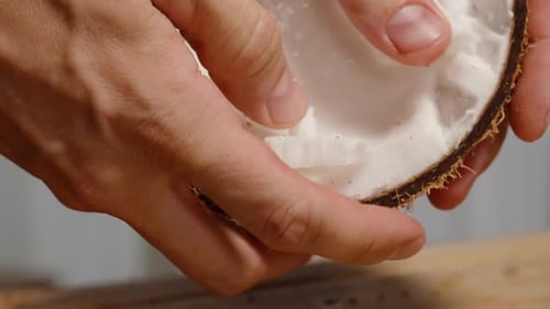Attempts to Pry Out White Coconut Pulp from the Shell with Hands. Close-Up.