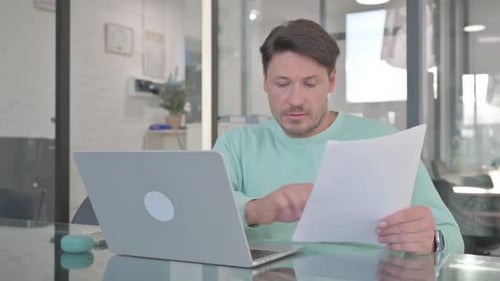 Man Working on Laptop with Documents in Office
