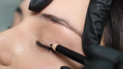 Un estilista aplica una máscara negra en las pestañas del ojo de una mujer Una cosmetóloga hace un maquillaje