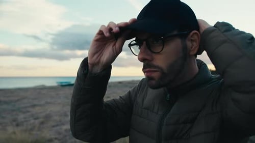 Man on Beach Puts on Baseball Cap