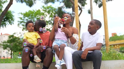 African black ethnic family with children in playground having fun blowing soap bubbles