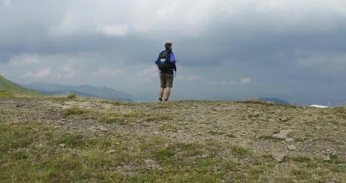 Aerial shot of a carefree man tourist with backpack is reached a peak while hiking on the path in