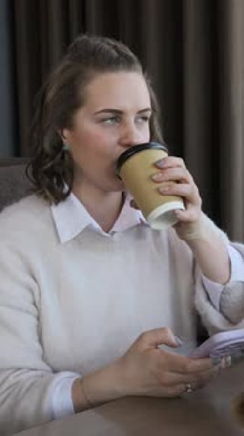 Young Woman Drinking Coffee and Texting on Smartphone in Cafe