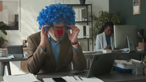 Empresário sobrecarregado com peruca de palhaço fazendo uma pausa durante o dia de trabalho no escritório