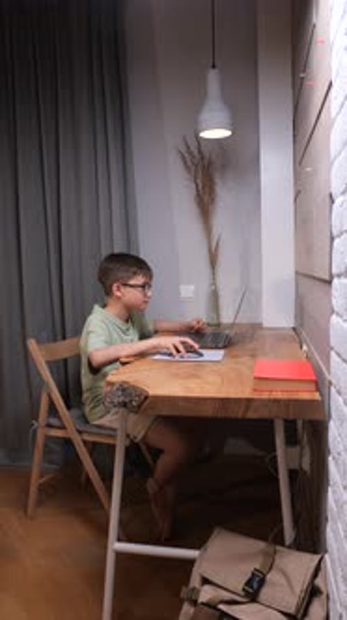 Vertical Video Young Boy Wearing Glasses Sitting at a Wooden Desk Using a Laptop and Trackpad While