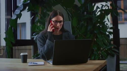 A Young Business Woman Makes a Call on Her Smartphone in a Modern Office with Plants