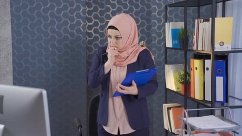 Muslim business woman in hijab takes and analyzes notes in office.