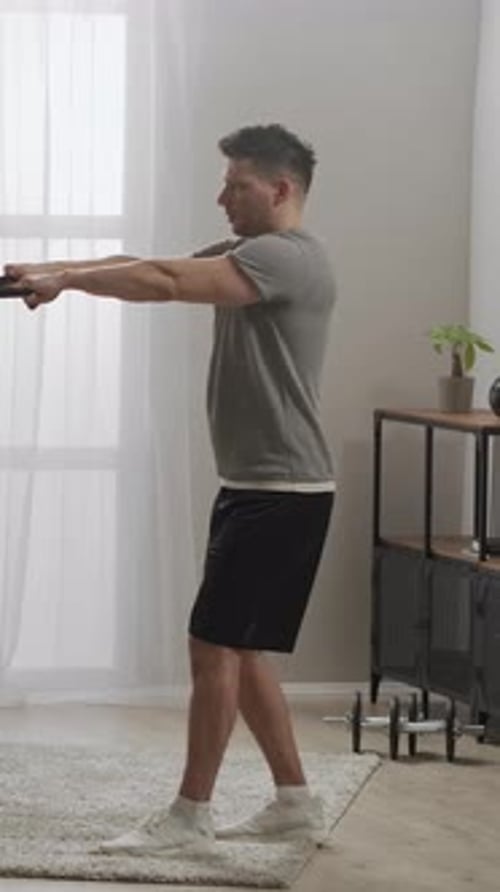 Focused Young Man Performing Resistance Band Workout at Home Exercising Arms and Shoulders with