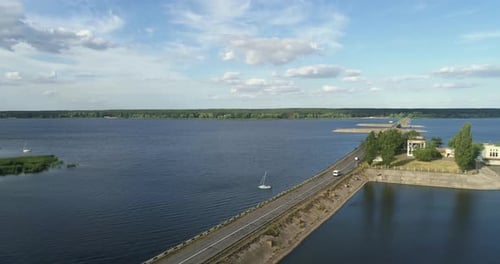 Cars Drive on Road Through Water Storage Ponds in Rural Area